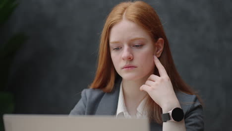 young-intern-lawyer-woman-is-reading-agreement-and-report-in-laptop-portrait-of-pretty-serious-lady-with-redhead-in-office